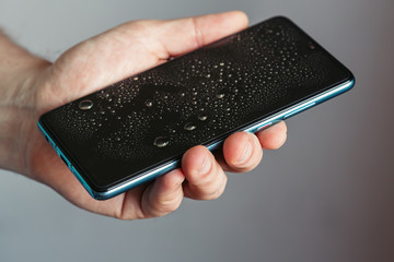 Drops on the glass of a smartphone screen, waterproof phone. man holds wet phone in his hand