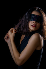 Fototapeta premium Portrait of beautiful young woman tying her eyes with black scarf on black background