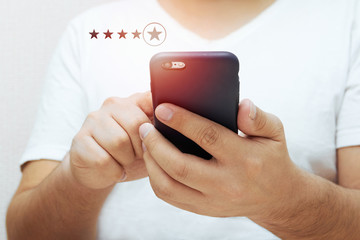 Close-up of a man's hand tapping on a smartphone screen with icons of a five-star rating of business service feedback and services. The client gives a rating