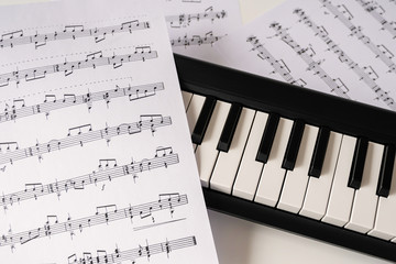 Selective focus of home synthesizer with sheet music (musical) notes on a white table. Piano...
