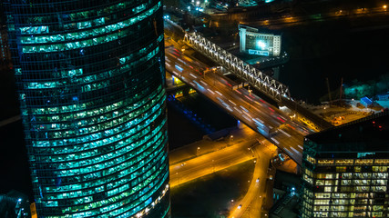 Fototapeta na wymiar Aerial view on glass skyscraper, fast moving cars traffic and warm illumination on Moscow city street at night. Rush hour, urban, transportation and city life concept
