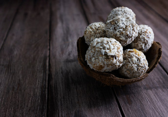 Homemade raw chocolate truffles with nuts and chia seeds in coconut flakes on a wooden background, energy ball healthy sweets, copy space.