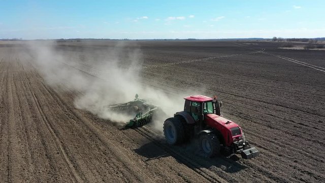 Tractor in the dust working in the field. Farmer seeding crops at field. Farmer with a tractor on the agricultural field sowing. aerial view by drone
