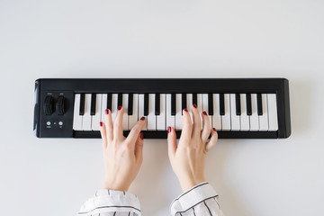 Woman hand playing on a home synthesizer on a white table. Piano keyboard. Flat lay.