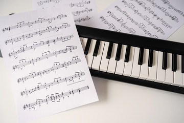 Selective focus of home synthesizer with sheet music (musical) notes on a white table. Piano keyboard.