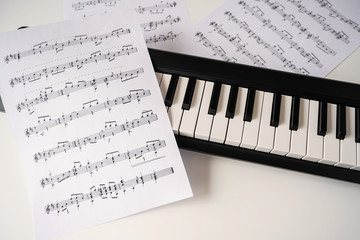 Fototapeta premium Selective focus of home synthesizer with sheet music (musical) notes on a white table. Piano keyboard.