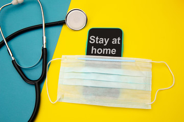 Stay at home - advice in mobile phone under face mask near stethoscope. Pandemic Covid-19 Coronavirus quarantine concept.