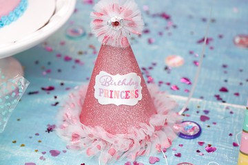 A closeup view of a girl's party hat that says Birthday Princess, on a table with glitter and sequins.