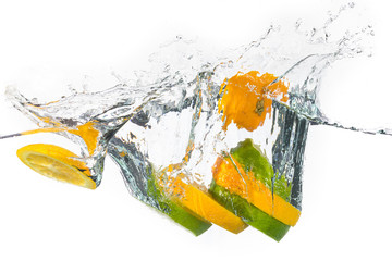 Slices of yellow and green lemon splashing on water in a white background