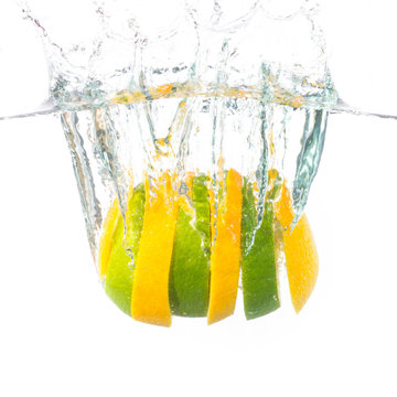 Slices of yellow and green lemon splashing on water in a white background