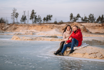 Lovers in down jackets walk on the ice of sand pits