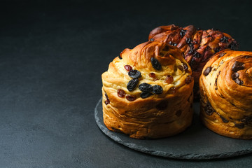 Cruffins with dried fruits, chocolate and black currants on a dark background.