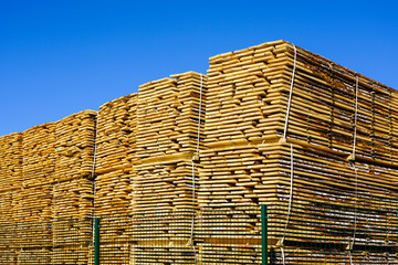 large stacks of wooden planks at the sawmill yard on the blue sky background