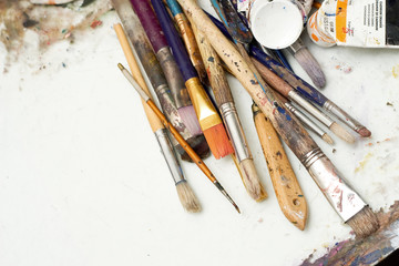 Several used and stained paintbrushes laying down in an artist studio tabletop.
