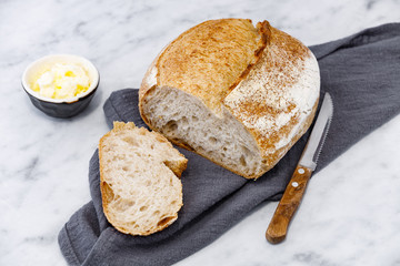 Crusty loaf of sourdough bread with jar of butter over modern napkin. Rustic breads on marble surface.  