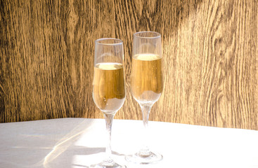 Two glasses of champagne. Glass goblets with alcohol on background of wooden wall. White linen tablecloth. Selective focus image. Copy space.