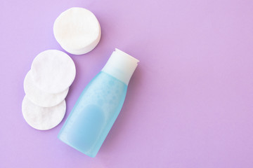 Top view of facial toner and round cotton pads on purple background with copy space. Blue liquid tonic or make up remover for face care
