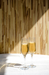 Two glasses of champagne. Glass goblets with alcohol on background of wooden wall. White linen tablecloth. Selective focus image. Copy space.