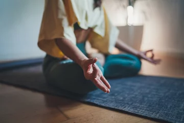 Tuinposter Home Yoga Flow, Closeup of young woman making mindfulness meditation at home sitting in lotus pose on yoga mat focus on feelings at the moment © iana_kolesnikova