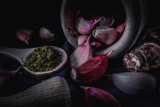 bodeg&oacute;n de ajo, perejil, con aceite y mortero en fondo negro.