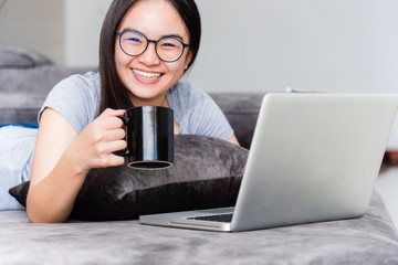 Portrait beautiful Asian young woman holding coffee cup smile and looking during a work, Cute girl teens happy on the sofa working remotely with a laptop and inteWoman holding coffee cup during a work