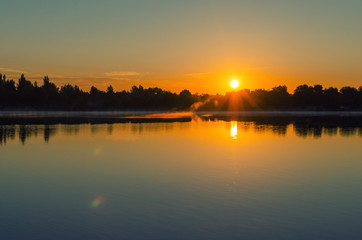 Fototapeta premium Dawn on the lake, the sun comes out of the trees