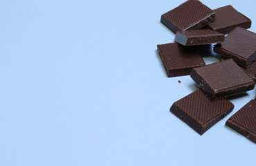 a bar of dark chocolate is broken into pieces, lies on a blue background. Place for text, inscriptions. Sweet life, international chocolate festival, sugar addiction, consumption
