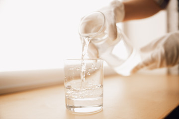 Close up of female hands in gloves holding bottle and glass, pouring pure water. Healthy lifestyle, health care, diet. Preparing, proposing for somebody. Copyspace. Water purification, safety.