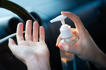 Close-up driver washing hands with alcohol gel to prevent infection corona virus covid-19. Steering wheel in the car in soft focus on background.