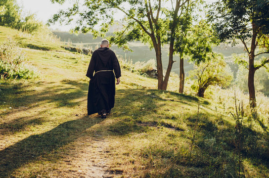 monk of the Capuchin Order, an adult wise man with a beard and in long dark brown clothing walks the stone path in the morning in nature