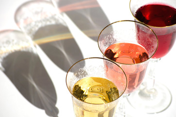 Top view. Flat lay. Three crystal glasses with white, red and rose wine. Glass goblets with alcoholol on white backgroundl. Direct sunlight, long shadows. Selective focus image. Copy space.