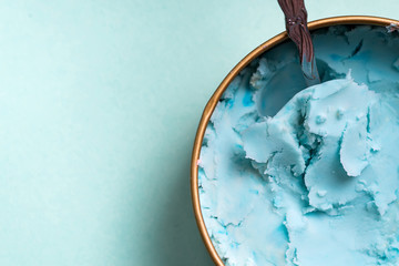 Fresh blue homemade natural ice-cream in a bowl with spoon on a light blue background.