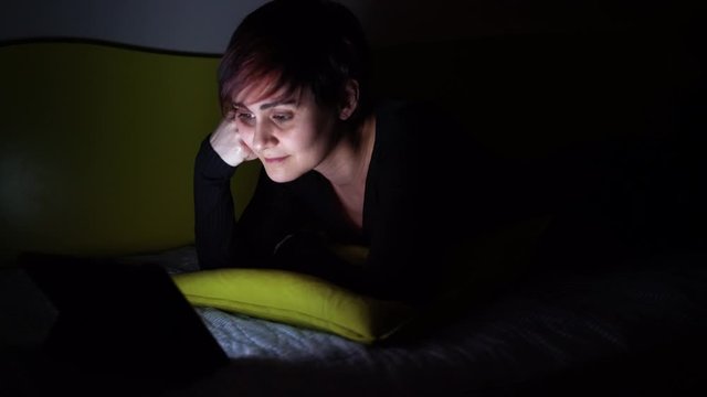 Young woman watching online tv show in bed at night. People hooked up with entertainment devices before going to bed. technology and leisure concept. Lifestyle at home for young people.