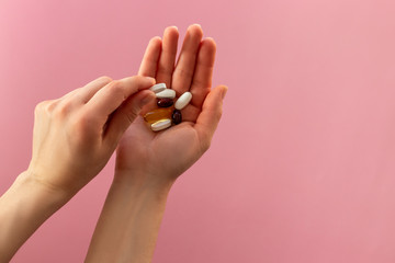 Woman holding pills on pink background. Copy space.