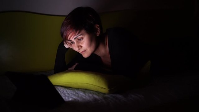 Young caucasian woman falling asleep watching tv in bed. People hooked up with entertainment devices before going to bed. technology and leisure concept. Insomnia and sleeplessness in bed concept.