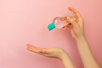 Women hands applying alcohol antibacterial sanitizer to prevent spread of bacteria and virus. Pink background with copy space.
