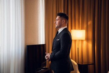 A young man in a fancy suit standing in a hotel room, looking into the window, meditating, preparing for a big day