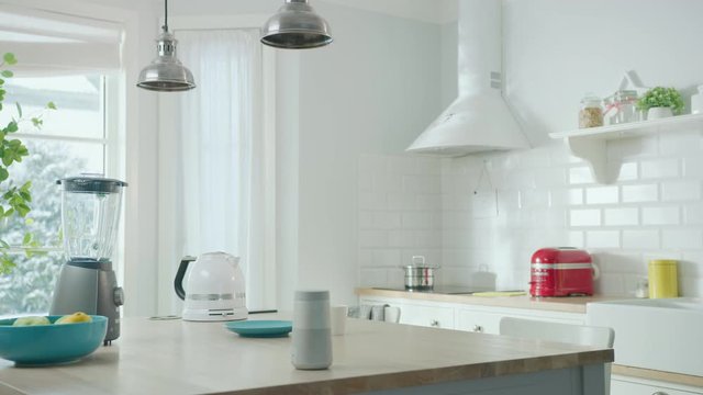 Cozy Modern Scandinavian Kitchen Interior with Electrical Appliances and Fruits. Empty Sunny Room with Wireless Speaker, Coffee Machine, Kettle and Toaster on a Wooden Table. Winter Snow Outside.