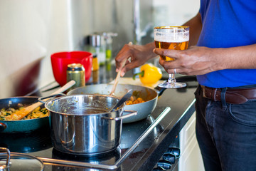 Man cooking on an electric stove in the kitchen while drinking a beer. Preparing food. Messy kitchen counter