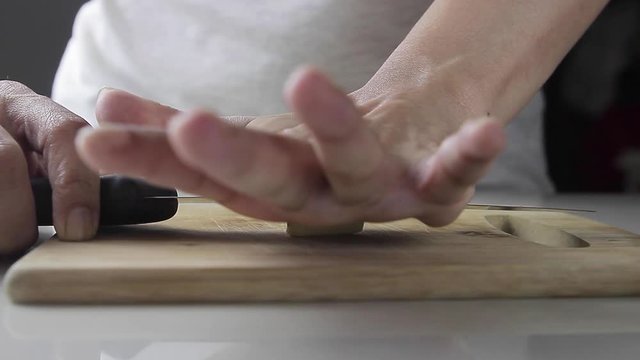 Closeup of a woman's hand crushing a garlic clove with knife on a wooden board