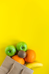 Delivery fruits, healthy food. Yellow background. Vegan vegetarian food - organic fruits in paper bag. Copy space. Grocery shopping food supermarket and clean eating concept.