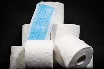 Close up detail on a pile of toilet papers with a hanging blue face mask
on the black background. The topic is about Corona virus - COVID 19