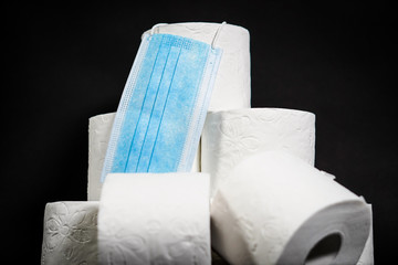 Close up detail on a pile of toilet papers with a hanging blue face mask
on the black background. The topic is about Corona virus - COVID 19
