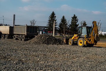 UKRAINE, LUTSK - April 10, 2020: Yellow wheel loader Excavator machine working at construction site with gravel. Preparing of the fundament for a asphalting. Road construction site.