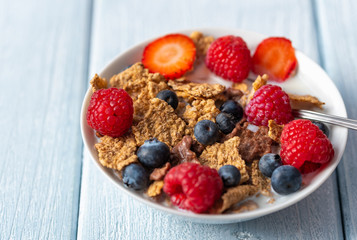 Granola with blueberries and raspberries in white bowl on dark white desk.