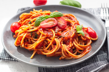 Pasta, spaghetti with tomato sauce, fresh tomatoes and basil in black ceramic plate. Grey stone background. Close up.