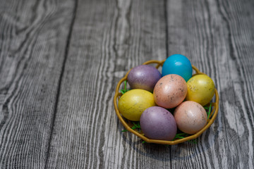 Obraz na płótnie Canvas A basket with many multi colored easter eggs on the wooden background.