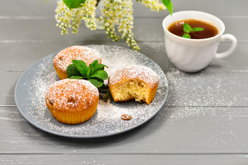 Composition with a cup of tea, cupcakes and white cherry flowers on a wooden background.