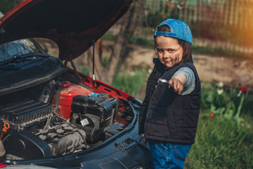 Little child trying to fix broken real car. Dreaming to be auto technician