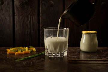 a glass of milk falling from a brown saucepan onto a wooden bottom with pasta and yogurt